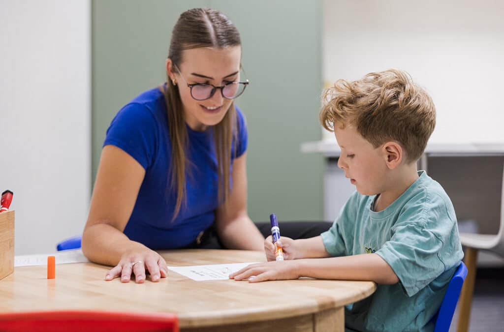 Speech pathologist supporting a young child with writing skills at a therapy table